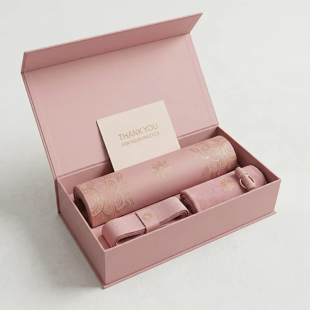 An open dusty pink gift box containing a rolled pink practice mat with gold foil detailing, a matching pink strap, a small pink container, and a thank-you card that reads 'THANK YOU FOR YOUR PRINCIPLE'.